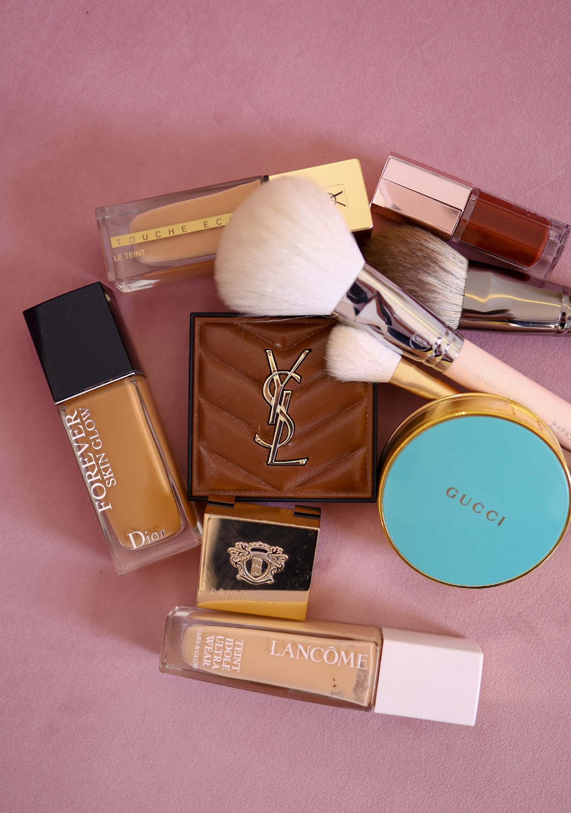 Kosmetyki do makijażu marek Dior, YSL, Gucci i Lancôme na pudrowym tle